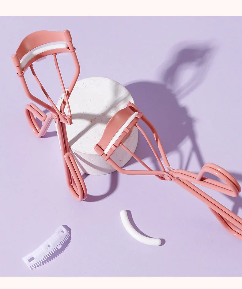 Recourbe-cils noir mat avec peigne séparateur intégré et coussinet en silicone rouge.
