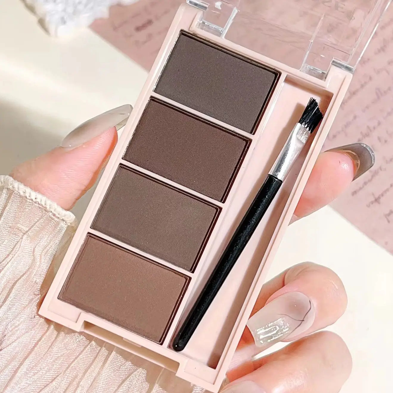 Palette de 4 poudres à sourcils mates (dégradés de gris et marron) avec ses pinceaux applicateurs intégrés.